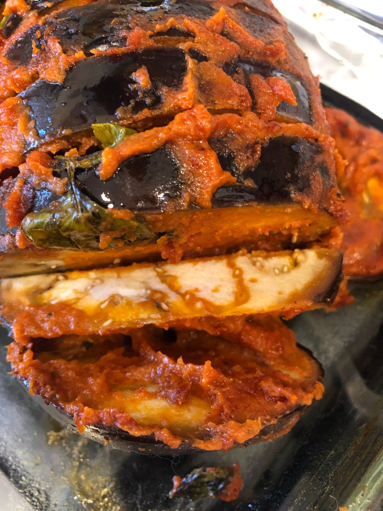 an eggplant covered in the red sauce, and a piece cut to show the inside is still white and hard